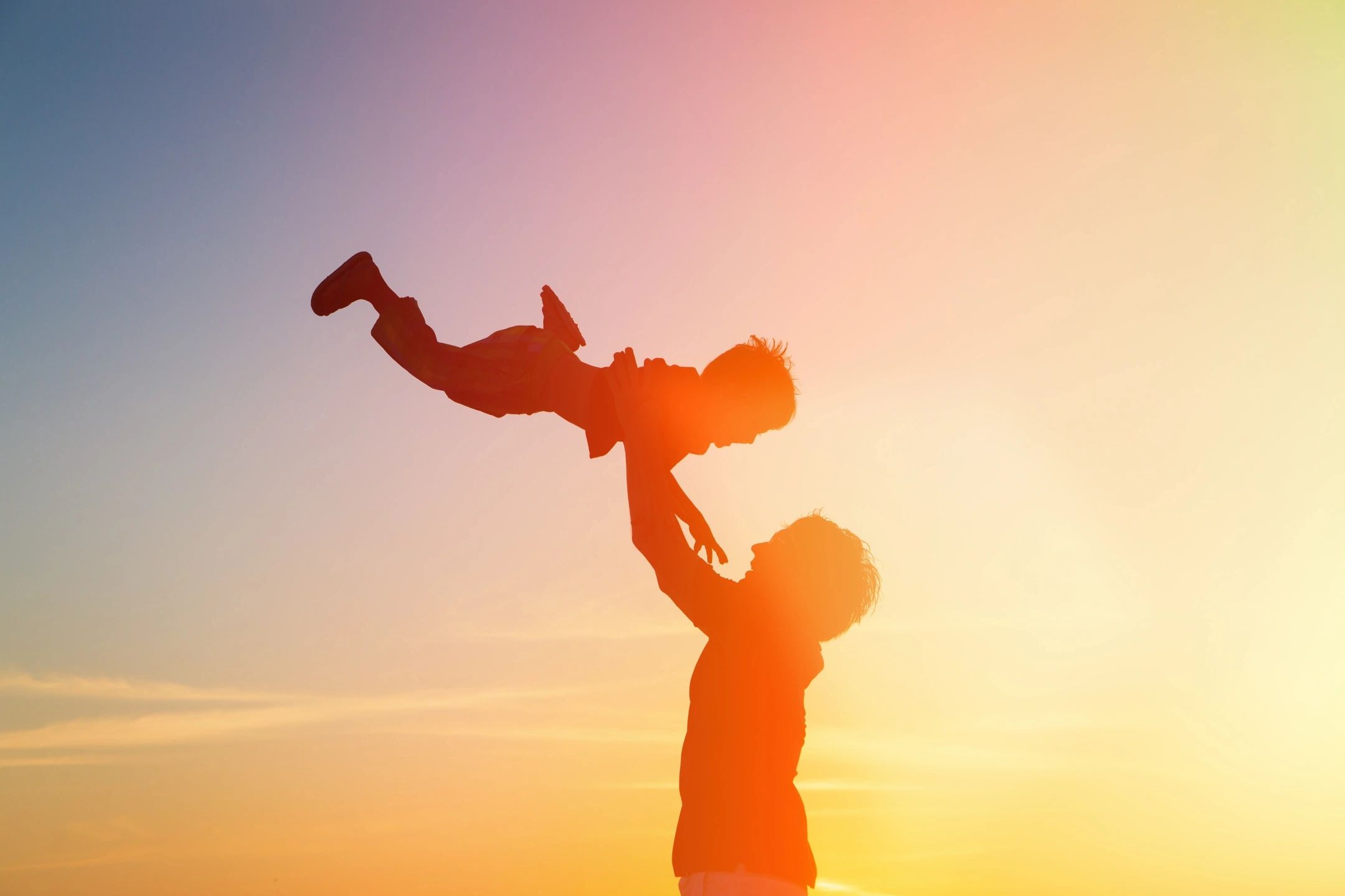 Playful parent tossing child silhouette at sunset