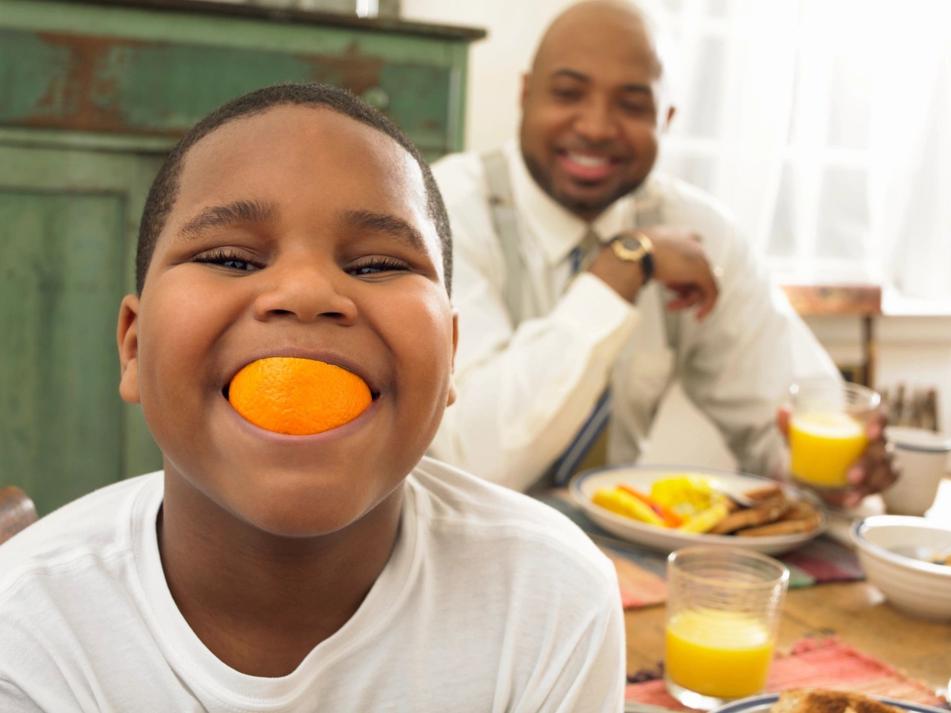 Boy with orange slice in mouth at breakfast